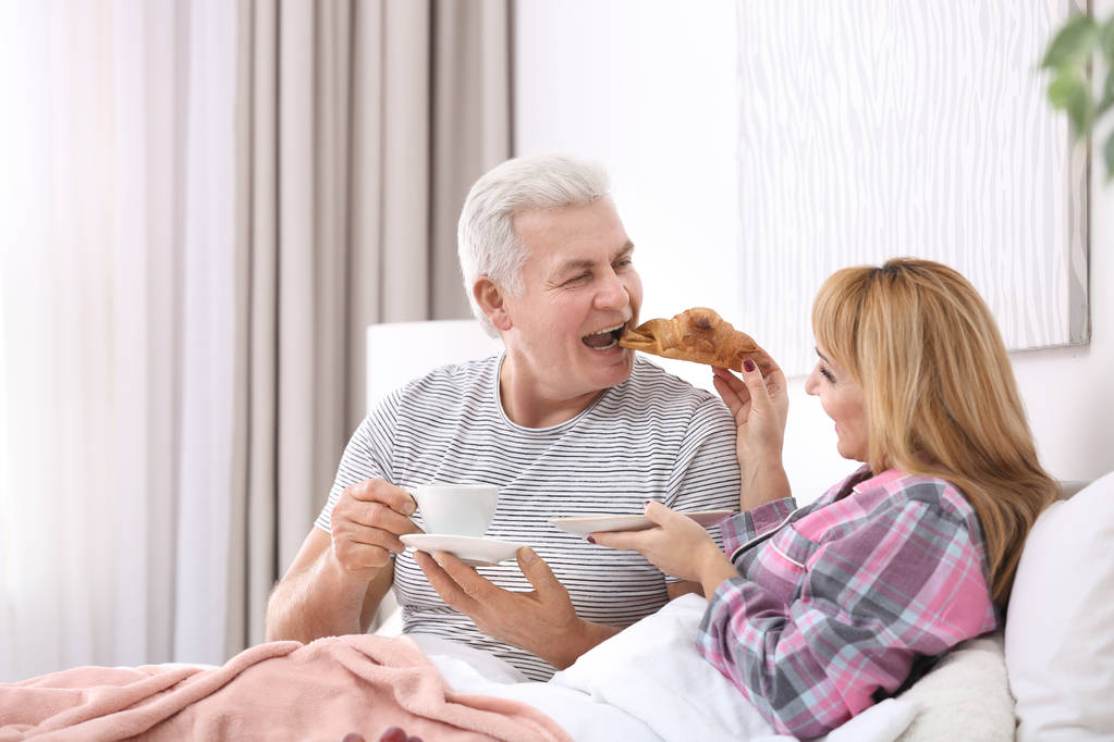大人のカップルがベッドで朝食を持っています。ロマンチックな朝 - 写真・画像