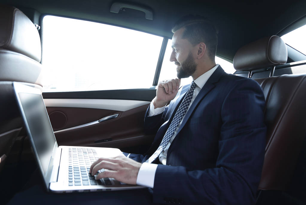 Uomo d'affari digitando testo sul computer portatile mentre seduto in auto
 - Foto, immagini