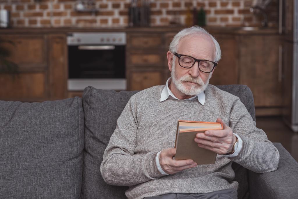 красивый пожилой человек, сидящий на диване и держащий в руках книгу
 - Фото, изображение