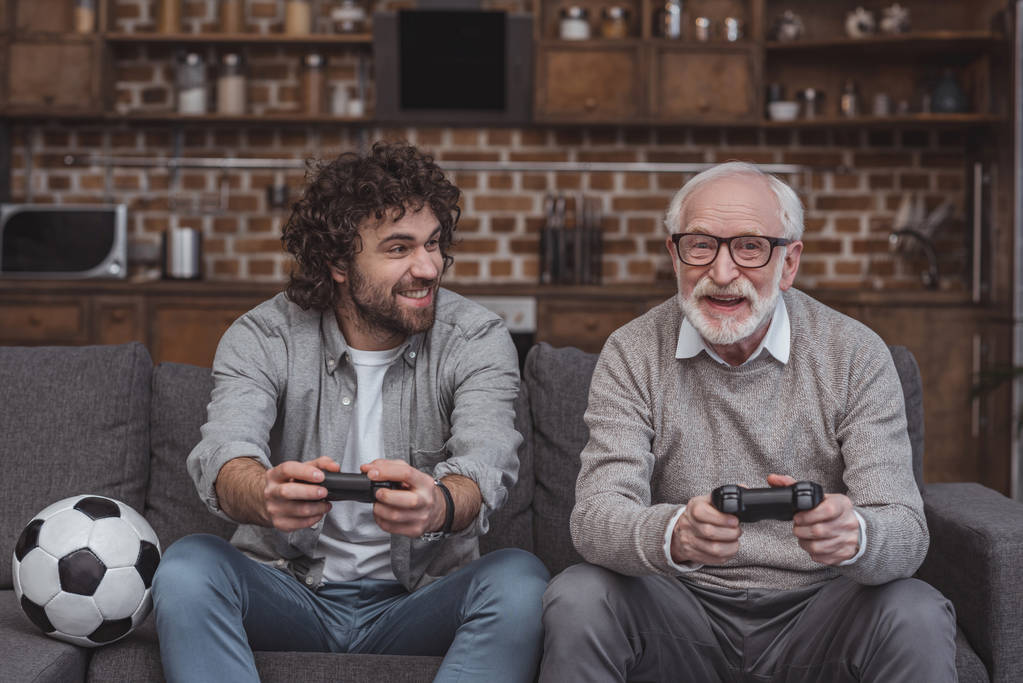 feliz filho adulto e pai sênior jogando videogame juntos em casa
 - Foto, Imagem