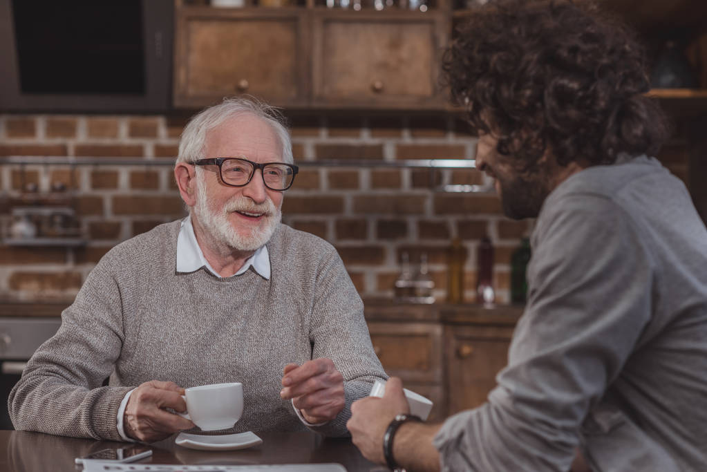 dorosły syn i starszy ojciec rozmowy i picia kawy w domu - Zdjęcie, obraz