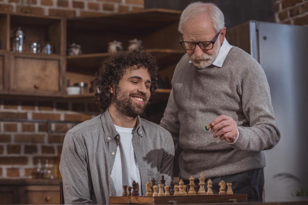 s úsměvem dospělého syna a starší otec hrál šachy doma - Fotografie, Obrázek