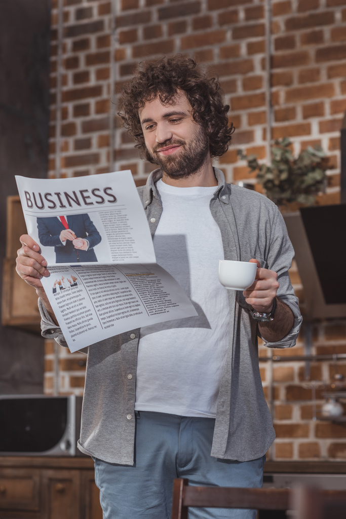 ハンサムな男の一杯のコーヒーを保持していると、家庭で新聞を読む - 写真・画像