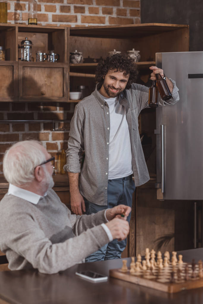 дорослий син пропонує пиво старшому батькові вдома
 - Фото, зображення