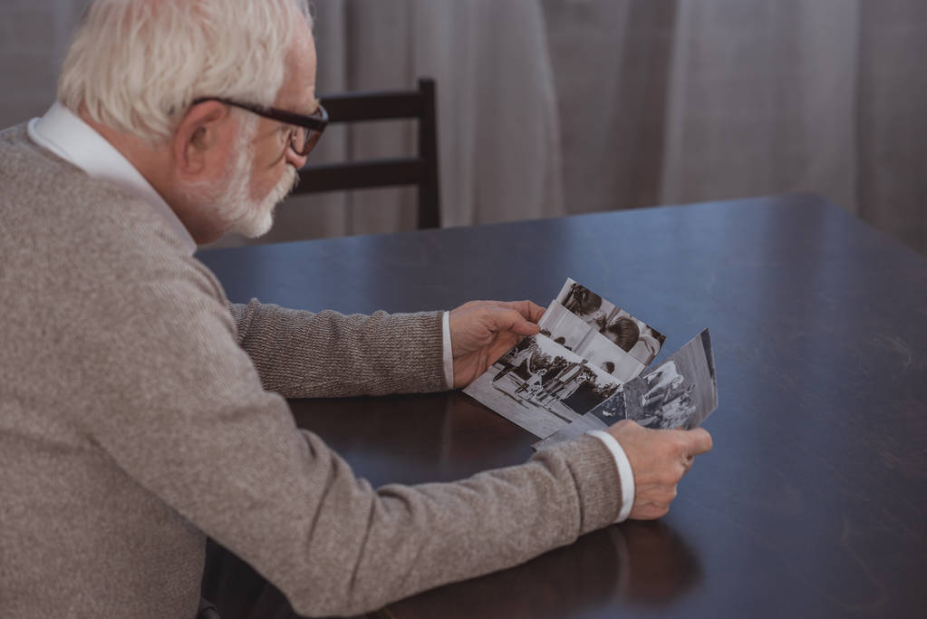vista lateral do homem de cabelo cinza sentado à mesa e olhando para fotos em casa
 - Foto, Imagem