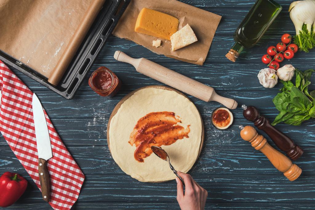 обрезанный образ женщины кладет томатную пасту на тесто для пиццы
 - Фото, изображение
