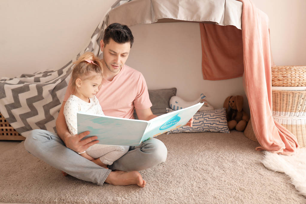 Father and his daughter reading book on floor in children room - Photo, Image