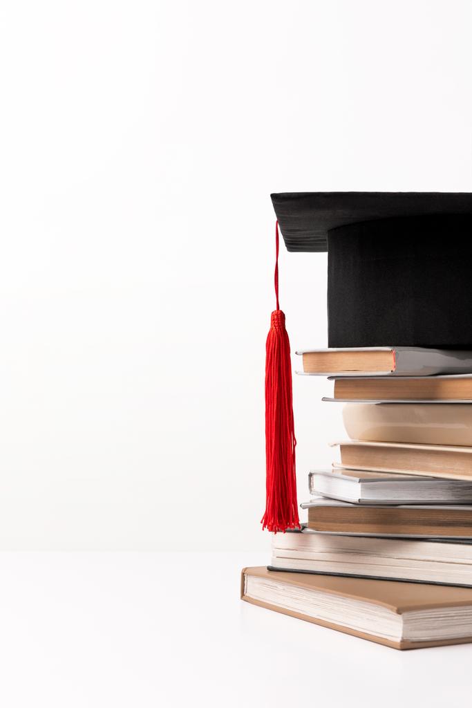 Sombrero académico sobre pila de libros aislados sobre blanco
 - Foto, Imagen