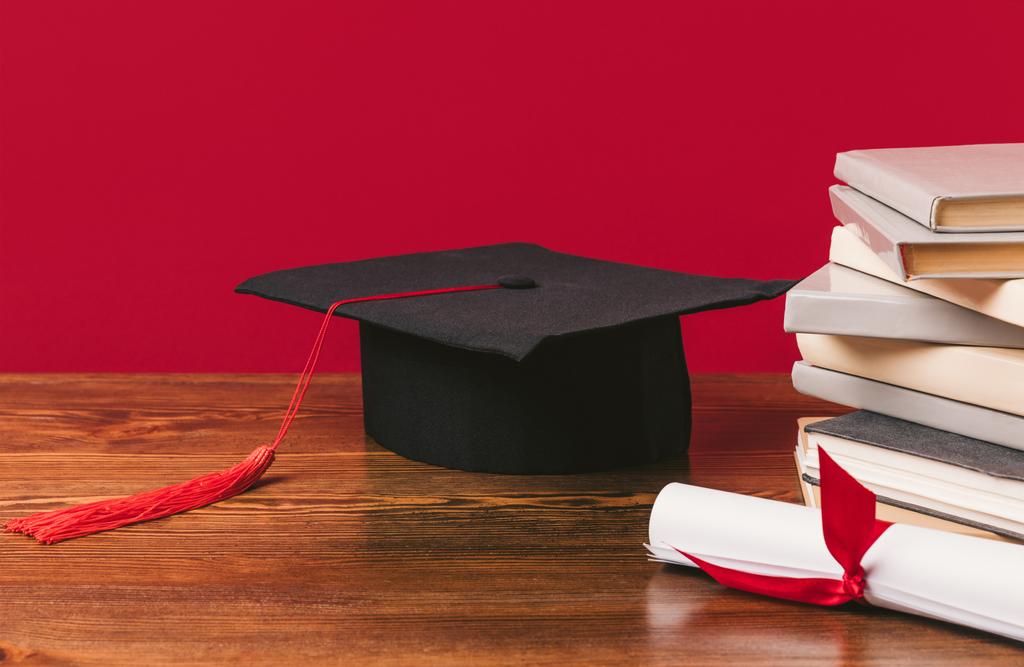 abgeschnittenes Bild eines Bücherstapels mit Diplom und akademischer Mütze auf Rot - Foto, Bild