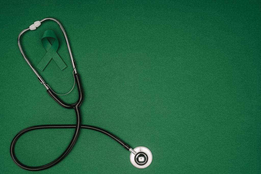Yeşil farkındalık şerit üstten görünüm skolyoz, ruh sağlığı sembolü ve yeşil yüzey üzerinde izole stetoskop - Fotoğraf, Görsel