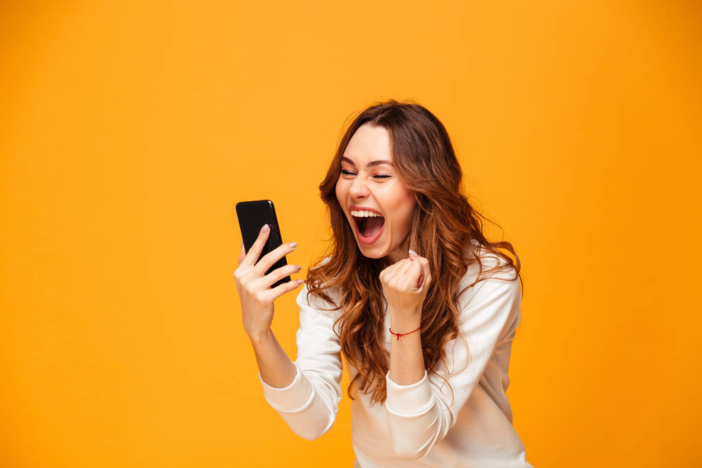 Joyeux cris femme brune en pull tenant smartphone et se réjouit
 - Photo, image