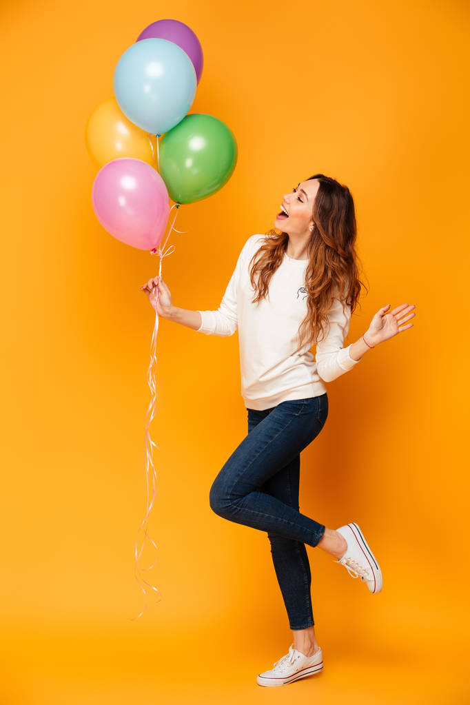 Volledige lengte beeld van gelukkige vrouw in trui houden ballonnen - Foto, afbeelding