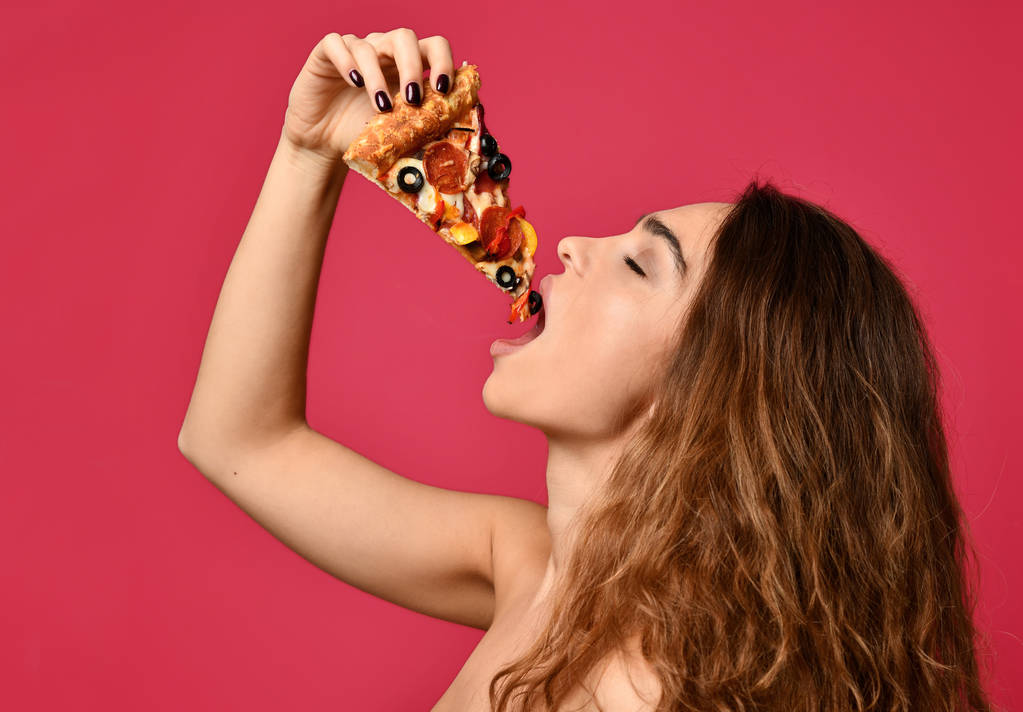 junge schöne Frau isst ein Stück Pfefferoni-Pizza lächelnd auf dunkelrot  - Foto, Bild