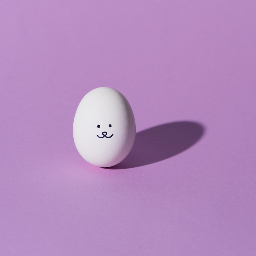 um ovo de galinha com smiley na superfície roxa
 - Foto, Imagem