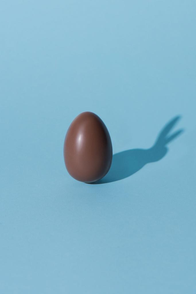 un huevo de Pascua de chocolate con sombra de conejo en la superficie azul
 - Foto, Imagen