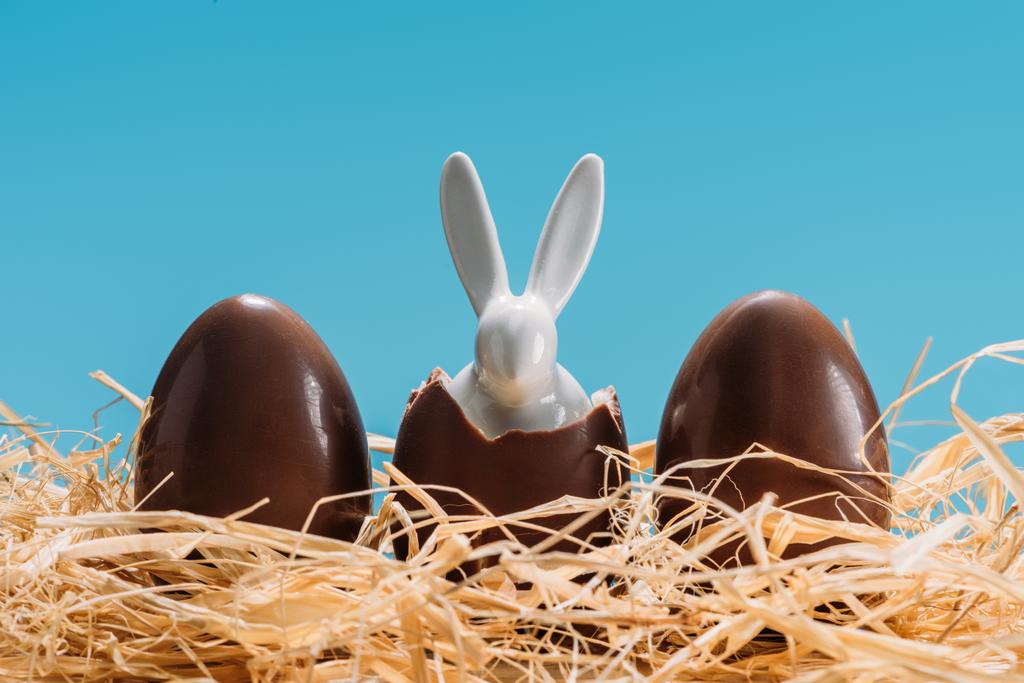 húsvéti nyuszi a csokoládé tojások szalmán elszigetelt kék - Fotó, kép