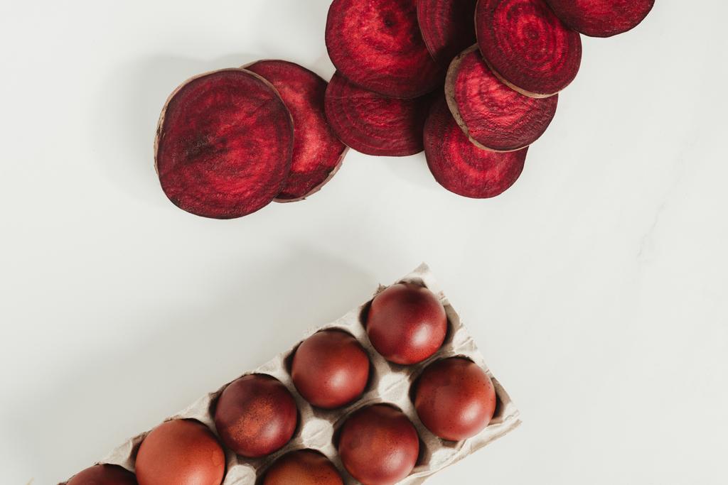 vista superior de huevos de gallina pintados en caja de huevos y rodajas de remolacha en gris
 - Foto, Imagen