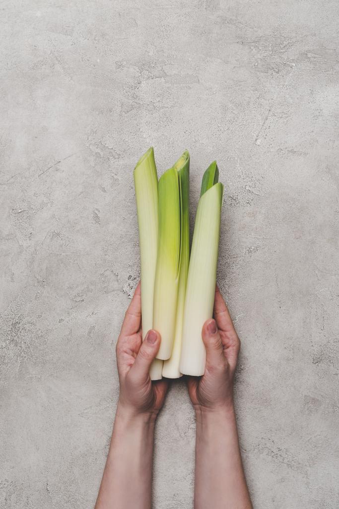 cropped shot of person holding fresh healthy leeks on grey - Photo, Image