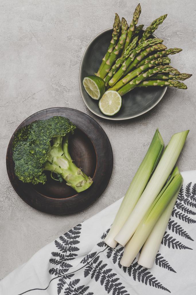 bovenaanzicht van verse gezonde groene groenten op platen en servet op grijs - Foto, afbeelding