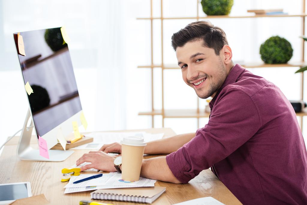 боковой вид улыбающегося менеджера по маркетингу, работающего за компьютером на рабочем месте в офисе
 - Фото, изображение