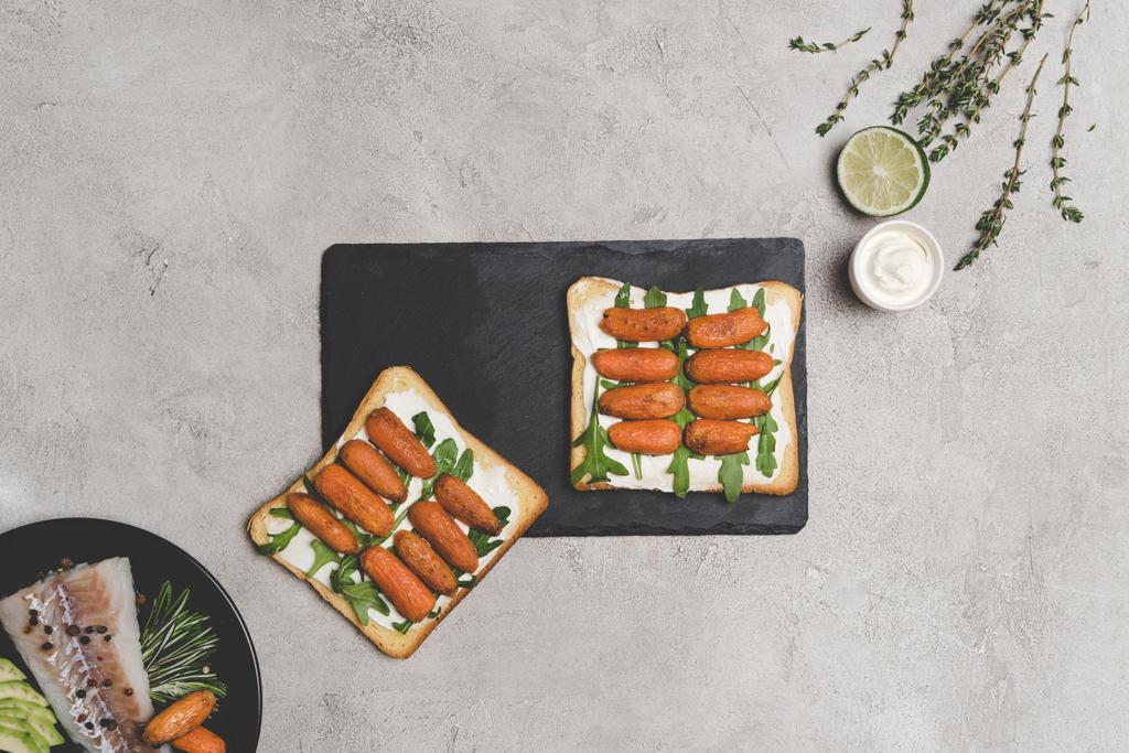 bovenaanzicht van gezonde sandwiches met baby wortelen en rucola op leisteen bord - Foto, afbeelding