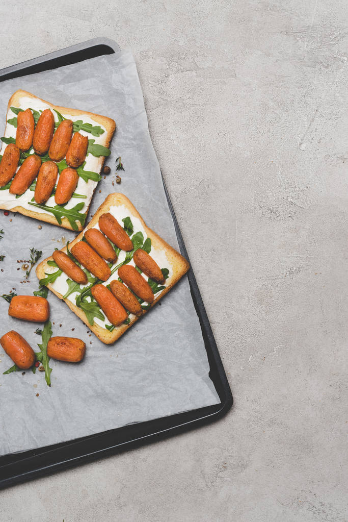 gezonde sandwiches met gebraden baby wortelen en rucola op bakken papier op grijs  - Foto, afbeelding