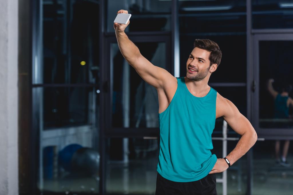 uśmiechający się sportowca biorąc selfie na smartfonie w siłowni - Zdjęcie, obraz