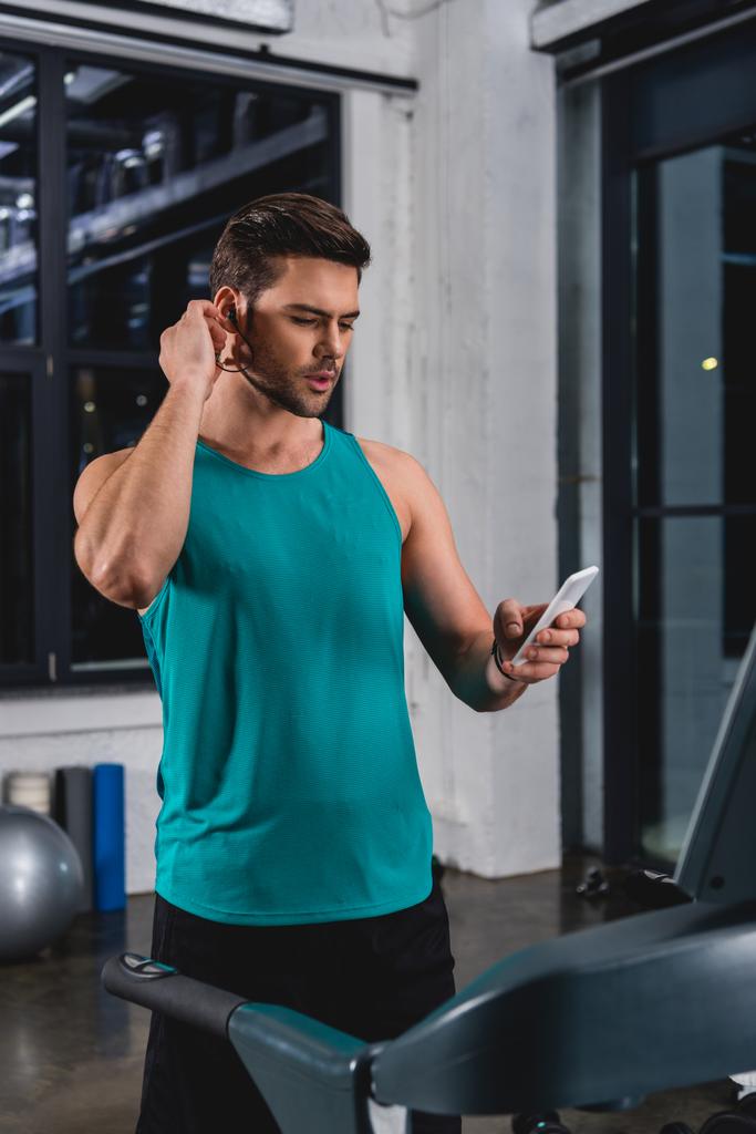 спортсмен слухає музику з навушниками та смартфон під час тренувань на біговій доріжці в спортзалі
 - Фото, зображення