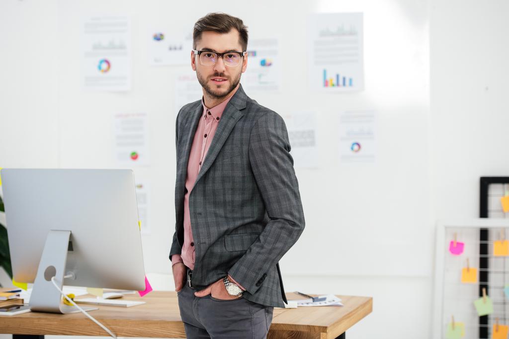 portrait of young businessman in suit and eyeglasses looking at camera at workplace in office - Photo, Image