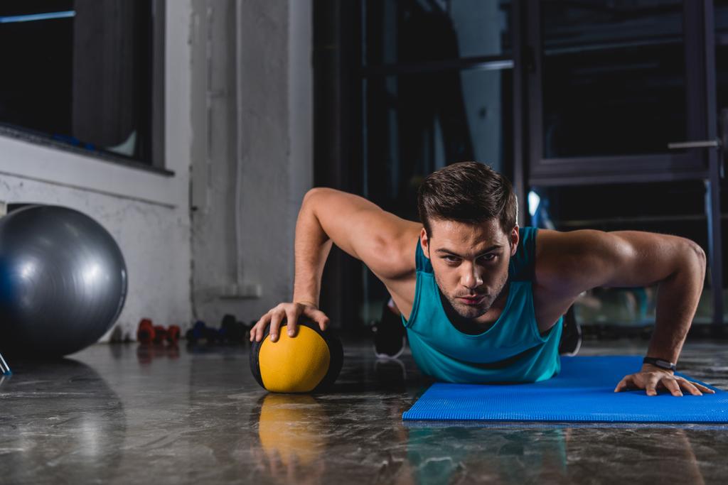 deportista haciendo flexiones con balón de medicina en estera de yoga en gimnasio
 - Foto, imagen