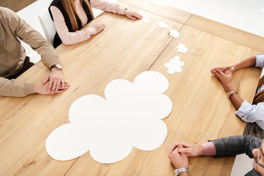 частковий вид на багаторасових ділових людей за дерев'яним столом з порожніми паперовими хмарами, концепція командної роботи
 - Фото, зображення