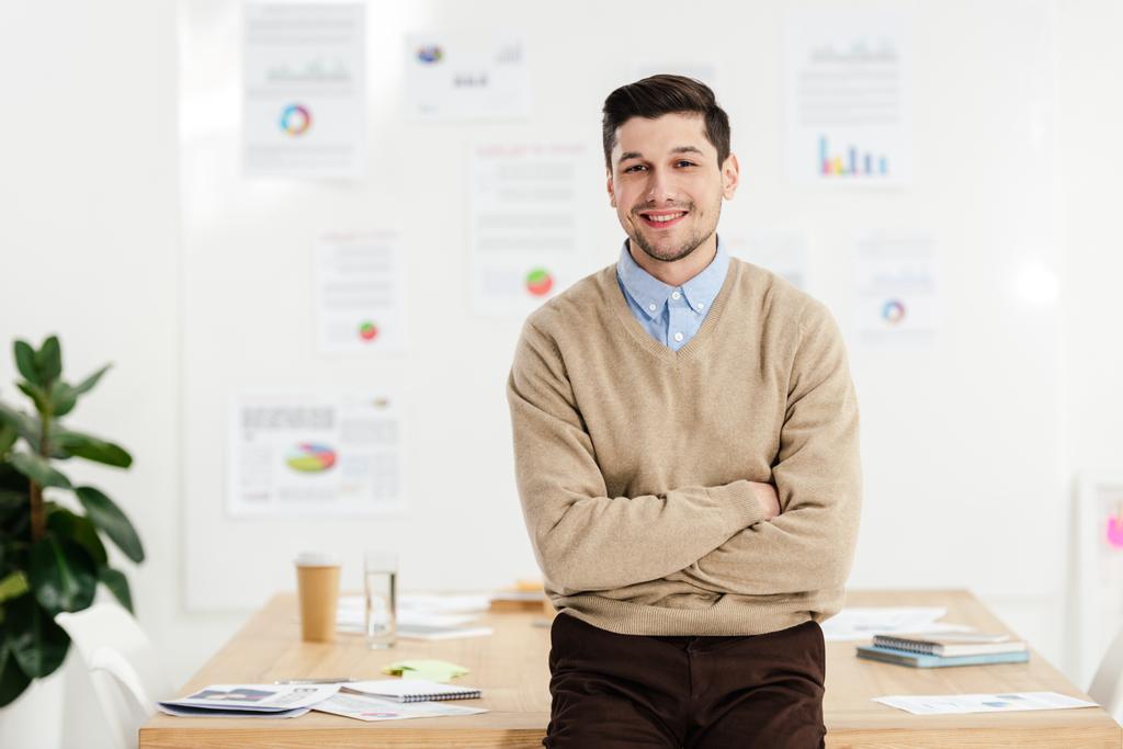 Portret van lachende marketingmanager met armen gekruist leunend op de werkplek op kantoor - Foto, afbeelding
