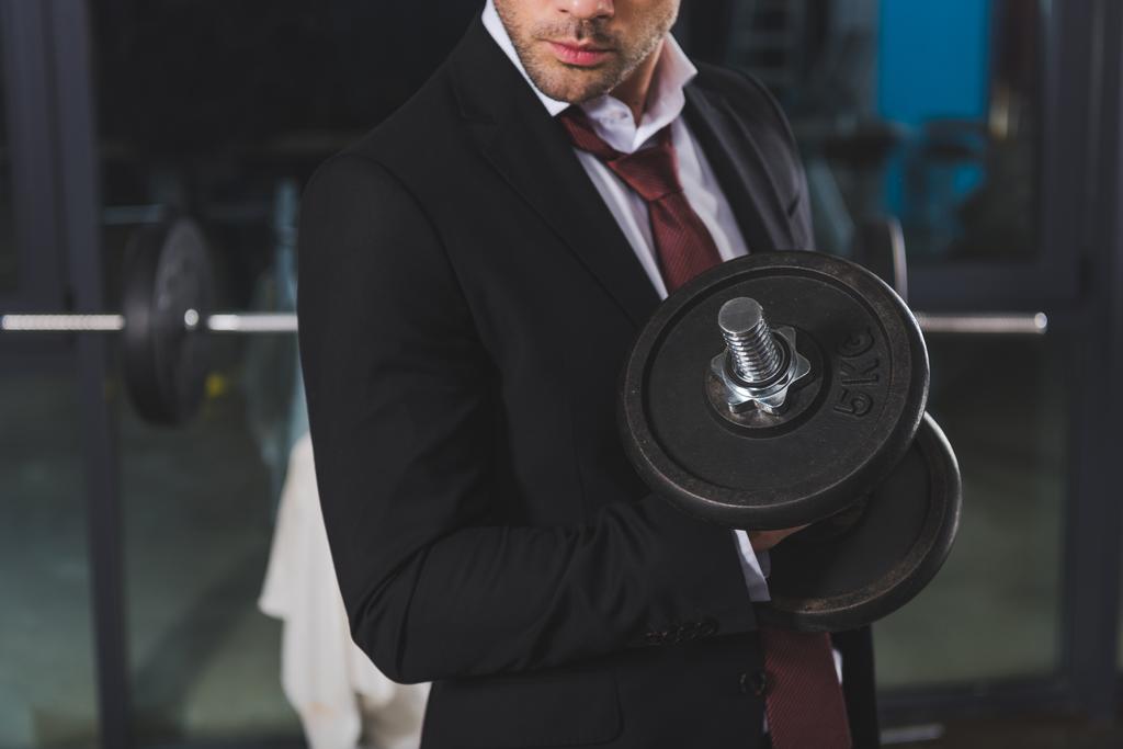 cropped view of sporty businessman in suit training with dumbbell in gym - Photo, Image
