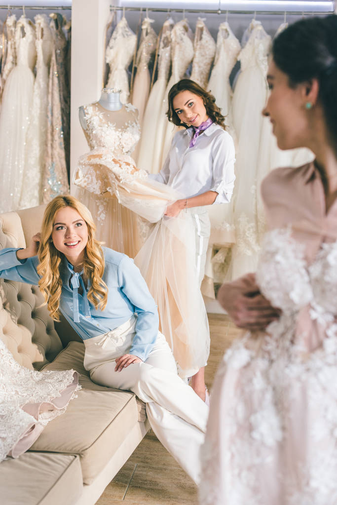 Щасливі жінки наречені намагаються на сукнях у весільному салоні
 - Фото, зображення