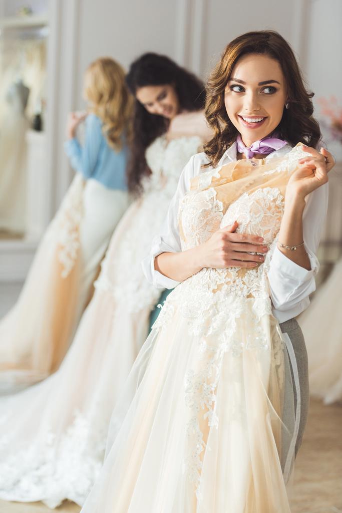 Lächelnde Frauen mit Brautkleidern im Hochzeitssalon - Foto, Bild