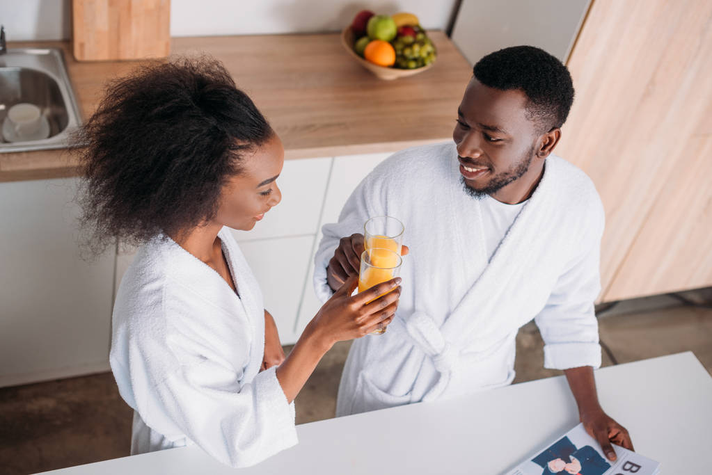 High angle view of couple clinking with glasses of orange juice in morning - Photo, Image