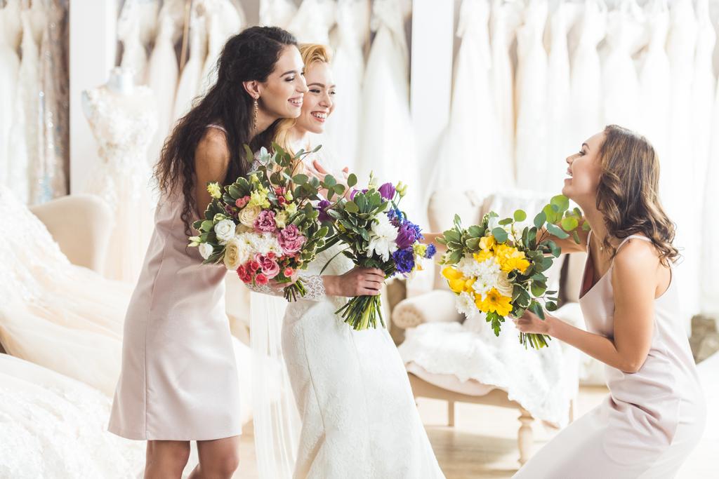 Νεαρή νύφη και παράνυμφων κρατώντας διαγωνισμού ανθοδέσμες από φρέσκα λουλούδια στο ατελιέ γάμου - Φωτογραφία, εικόνα