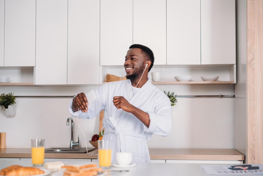 Africain américain dans les écouteurs écouter de la musique de smartphone et danser dans la cuisine
 - Photo, image