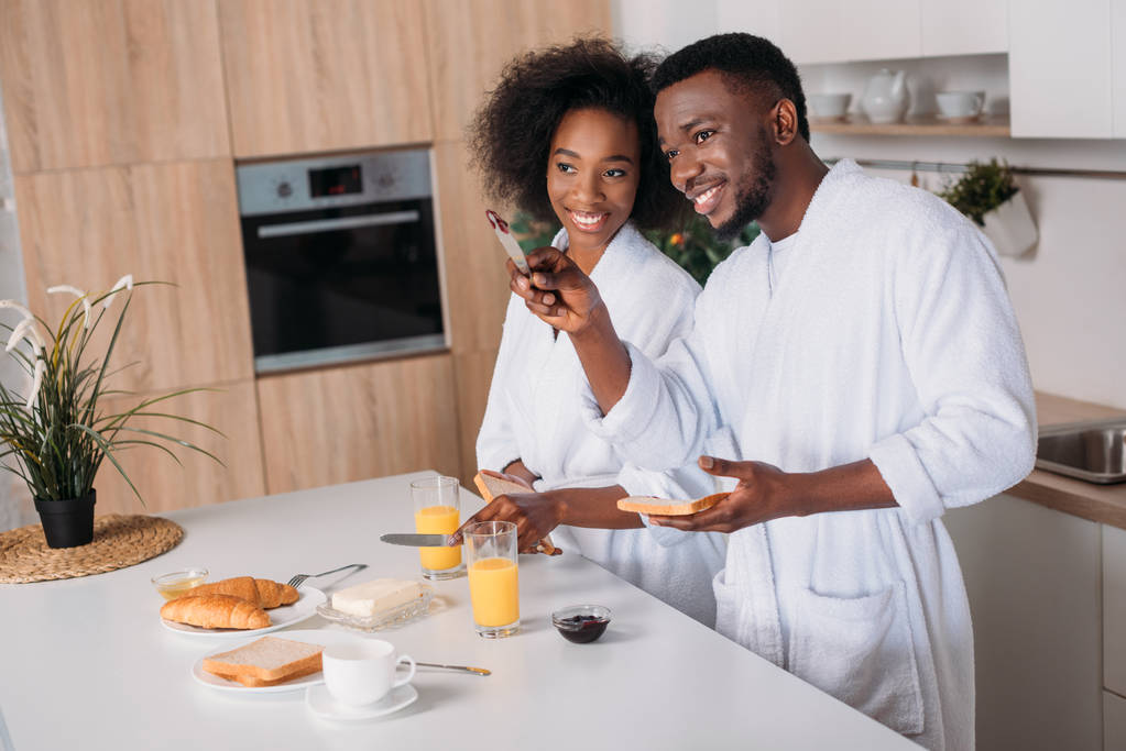 アフリカ系アメリカ人の台所で笑顔のガール フレンドを指す  - 写真・画像
