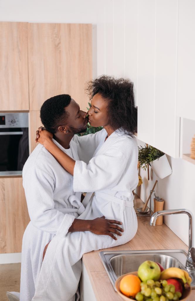 Vista lateral de pareja afroamericana besándose en cocina
  - Foto, Imagen