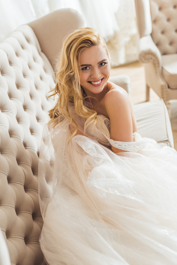 junge Braut im Tüllkleid auf Sofa liegend im Geschäft für Hochzeitsmode - Foto, Bild