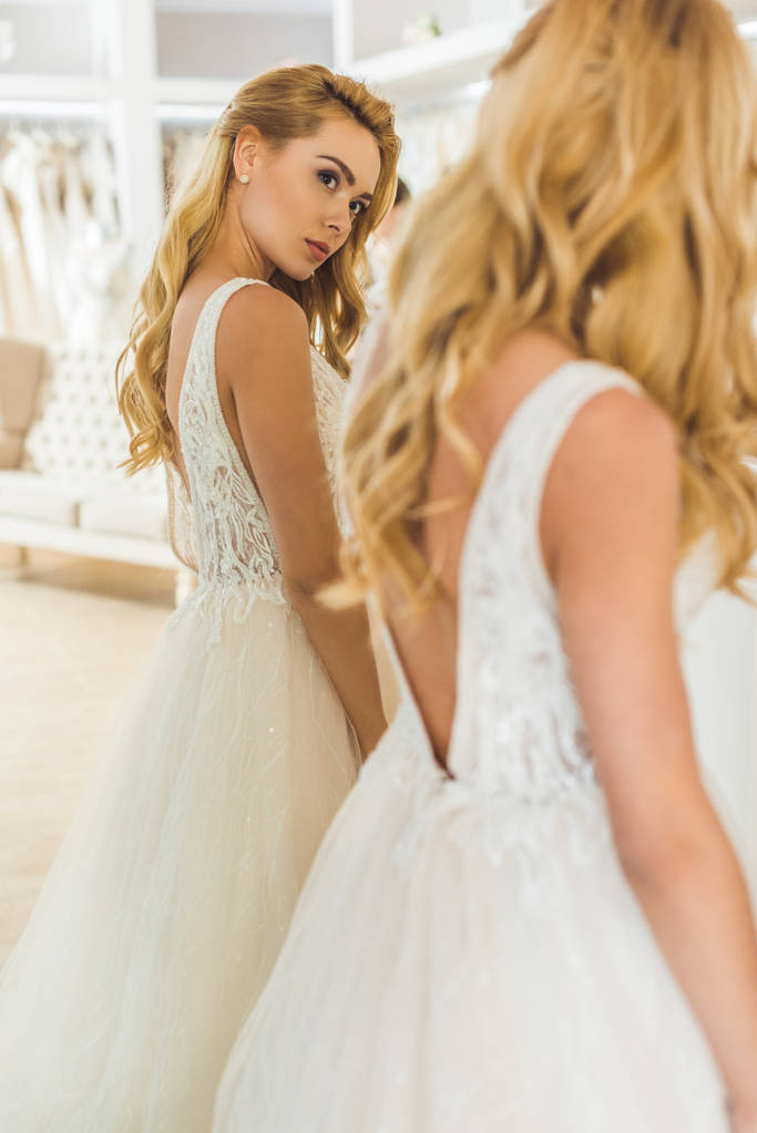 Jolie femme portant une robe de mariée par miroir dans un atelier de mariage
 - Photo, image