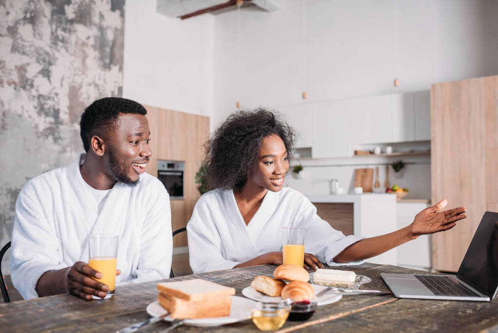 Jeune couple afro-américain assis à table avec ordinateur portable et petit déjeuner
  - Photo, image
