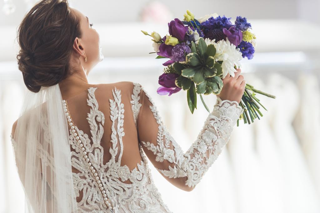 Rückansicht der Braut im Spitzenkleid mit Blumen im Geschäft für Hochzeitsmode - Foto, Bild