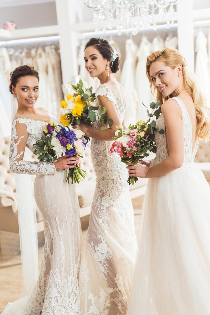 Привлекательные невесты, держащие букеты в свадебном ателье
 - Фото, изображение