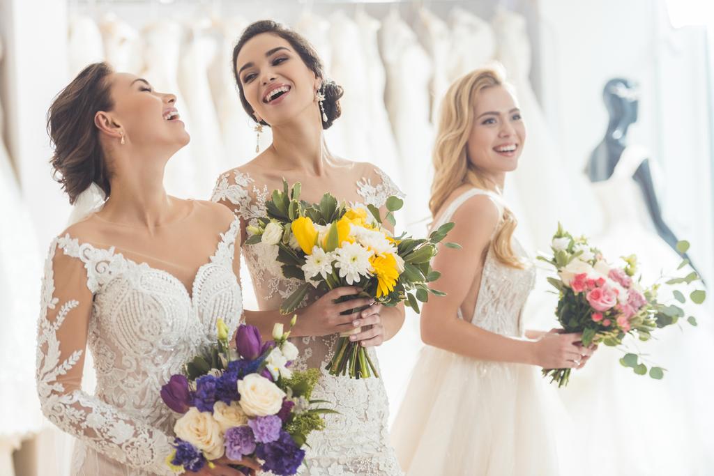 Gelukkig vrouwen in bruiloft jurken met bloemen in wedding atelier - Foto, afbeelding