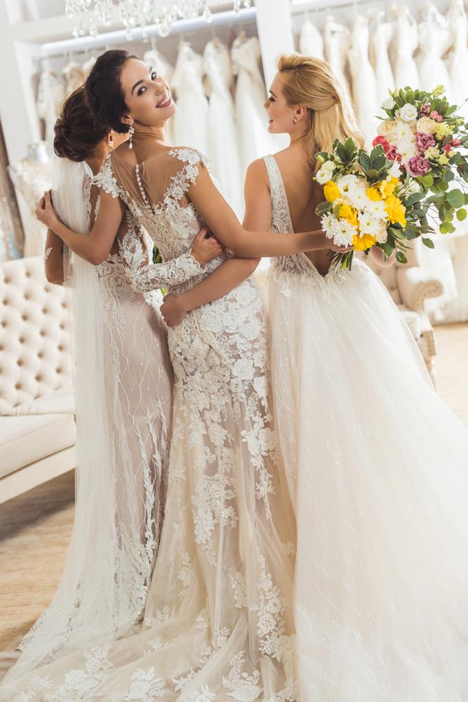 Молодые улыбающиеся невесты с букетами в свадебном ателье
 - Фото, изображение