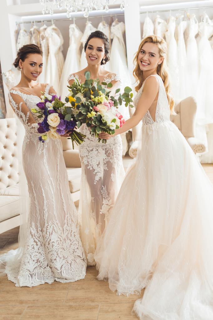 Gelukkig vrouwen in bruiloft jurken met bloemen in huwelijk salon - Foto, afbeelding
