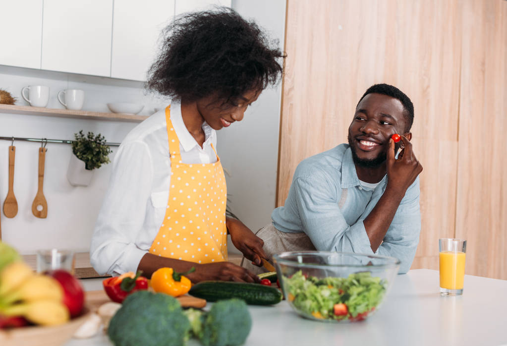 Улыбающаяся африканская американская пара в фартуках готовит на кухне
 - Фото, изображение