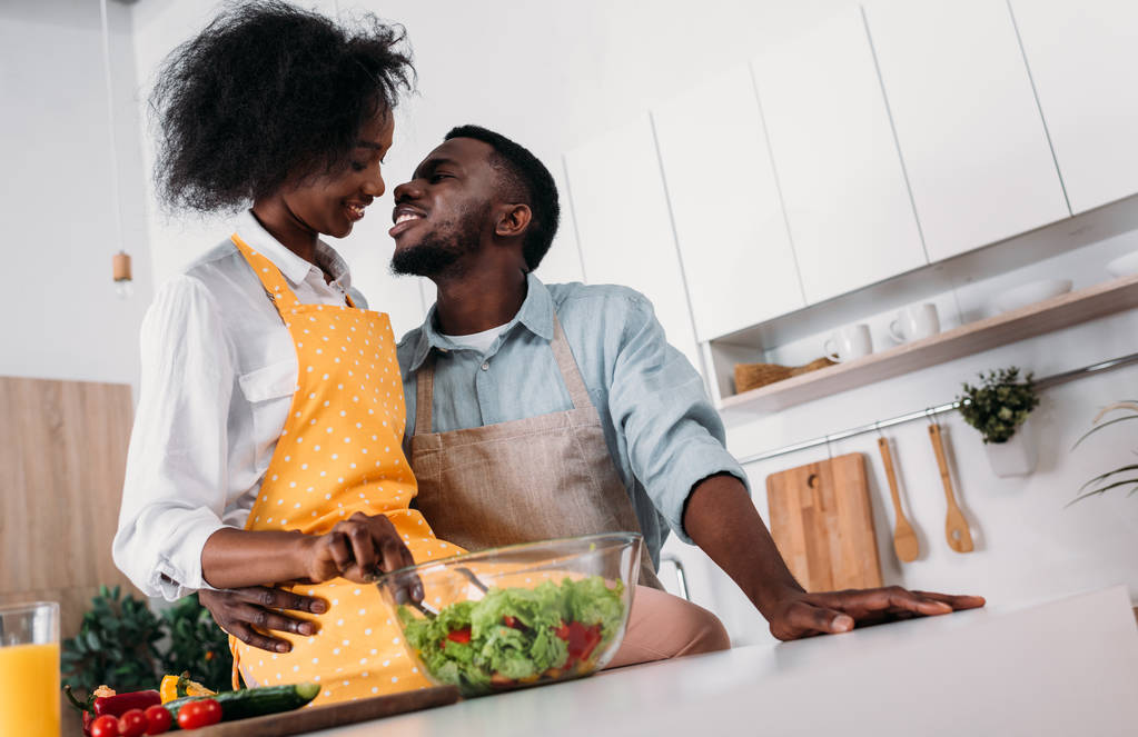 Low angle view of african american embracing and kissing in kitchen - Photo, Image